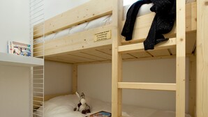 Une chambre avec un lit superposé en bois, une étagère avec un magazine et un jouet en peluche sur le lit du bas.