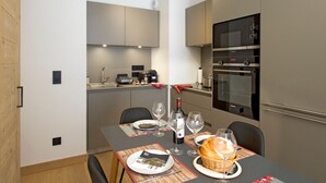 Une cuisine moderne dotée d’appareils électroménagers intégrés, une table à manger pour deux personnes et un petit îlot central agrémenté d’un panier de pain.