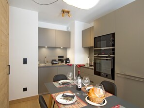 A modern kitchen with built-in appliances, a dining table set for two, and a small island with a basket of bread. - Bright apartment, ski-in/ski-out - 4 guests (Huez)