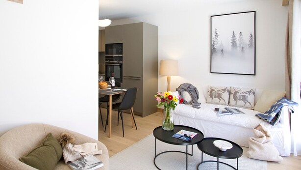 Un salon moderne avec un canapé, un coin repas avec des chaises, une table ornée d’un vase de fleurs et un tableau accroché au mur.