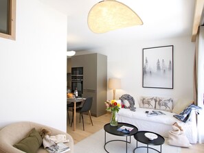 A modern living room with a sofa, a dining area with chairs, a table with a vase of flowers, and a painting on the wall. - Bright apartment, ski-in/ski-out - 4 guests (Huez)