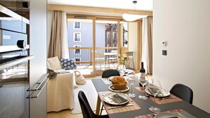 Un salon moderne comprenant un coin repas, un canapé, une table dressée pour deux personnes et une vue sur le balcon extérieur.