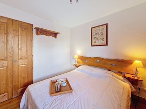 Ein Schlafzimmer mit einem hölzernen Kopfende, einem Nachttisch mit Lampe, einem Bett mit weißer Bettdecke, einem Holzschrank und einem Tablett mit Wasserkocher und Tassen.