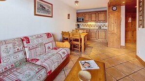 Un salon avec un canapé à motifs, une table à manger avec des chaises et une cuisine dotée de meubles en bois et d’un four à micro-ondes.