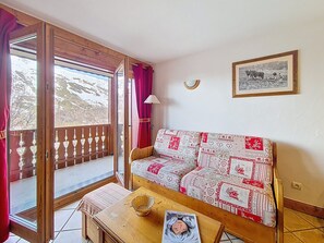 A cozy room with a wooden bench, a patterned sofa, a small table with a basket, and a framed picture on the wall. - Spacious apartment with balcony - 4 guests (Les Menuires)