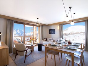 A modern hotel room with a dining area, a sofa, and a view of a snowy mountain. - Bright apartment, open view - 6 guests (Huez)