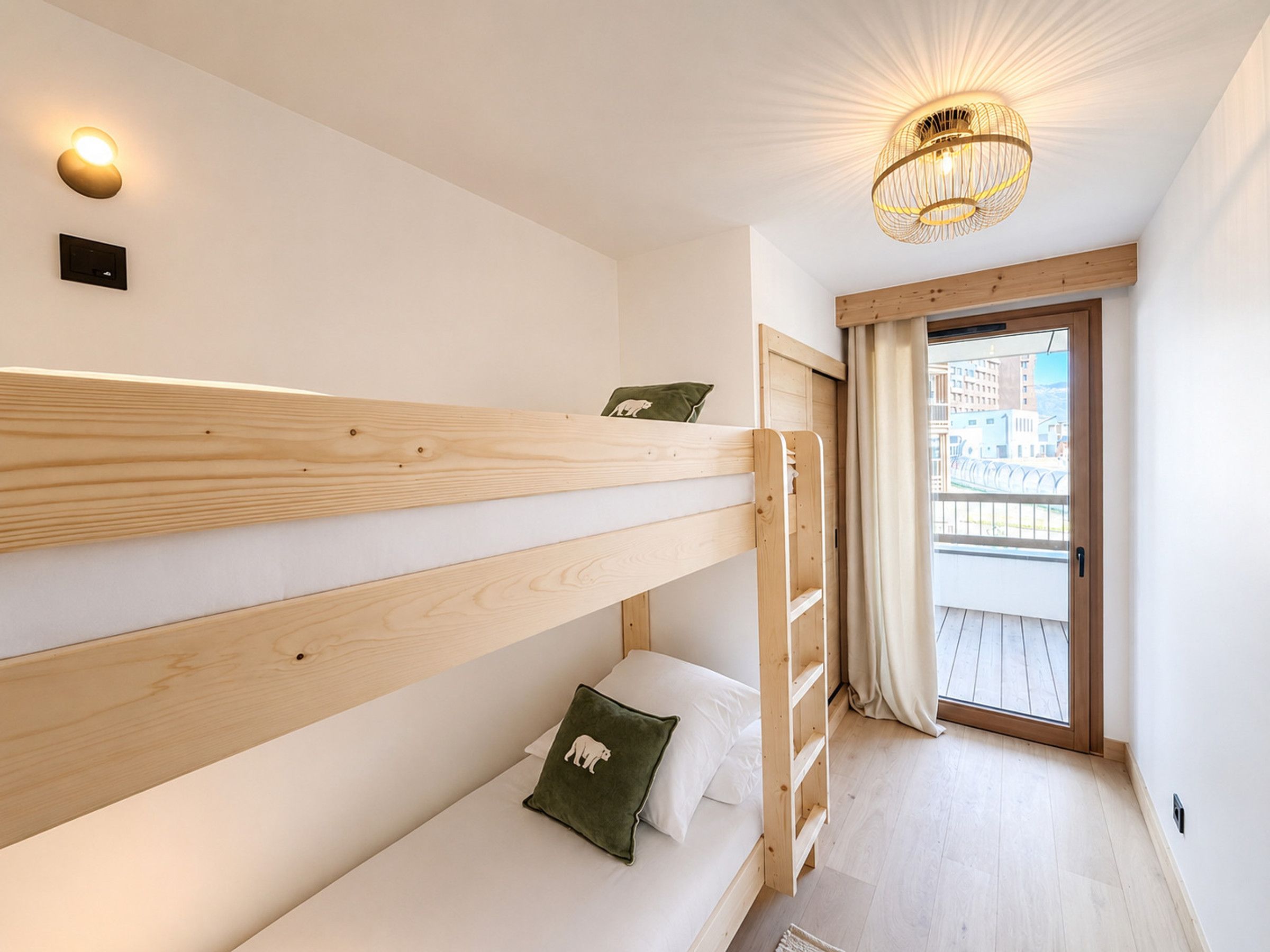 Habitación con literas, una escalera de madera, una ventana pequeña con cortinas y una lámpara en el techo.