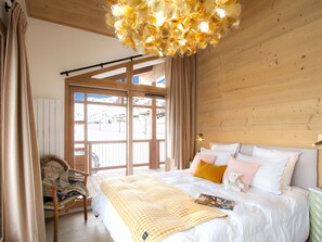 A bedroom with a large bed, a wooden ceiling, and a view of a snowy landscape through a large window. - Spacious apartment, slope view - 10 guests (Huez)