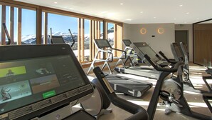A gym with treadmills and exercise equipment, large windows with a mountain view, and a digital screen displaying workout routines. - Spacious apartment, slope view - 10 guests (Huez)