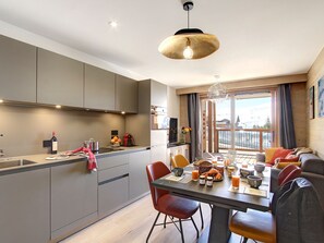 A modern kitchen with grey cabinets, a dining area with a table set for two, and a large window with curtains. - Bright apartment with south balcony - 4 guests (Huez)