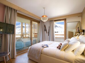 A bedroom with a large bed, a television, and a view of snowy mountains through the windows. - Stunning mountain apartment - 10 guests (Huez)