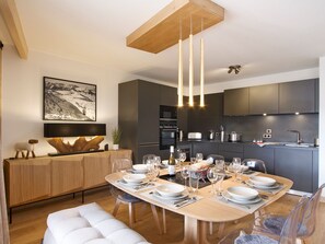 A modern kitchen with dark cabinets, a dining table set for six, and a wooden ceiling. - Stunning mountain apartment - 10 guests (Huez)