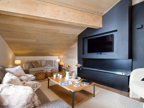 A modern living room with a wooden ceiling, a flat-screen TV mounted on a dark wall, a wooden coffee table, and a sofa with cushions. - Magnificent top-floor apartment - 8 guests (Huez)