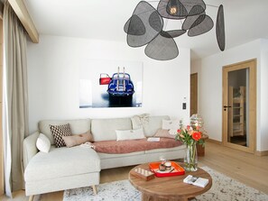 A modern living room with a sectional sofa, a round coffee table, and a wall-mounted light fixture. - Luxury apartment, station view - 6 guests (Huez)