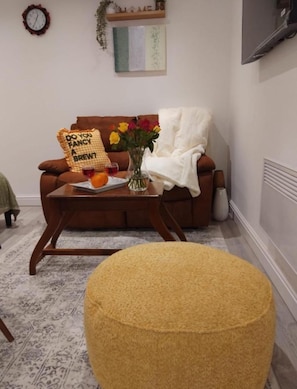 A living room with a brown sofa, a coffee table with a vase of flowers, and a yellow ottoman.