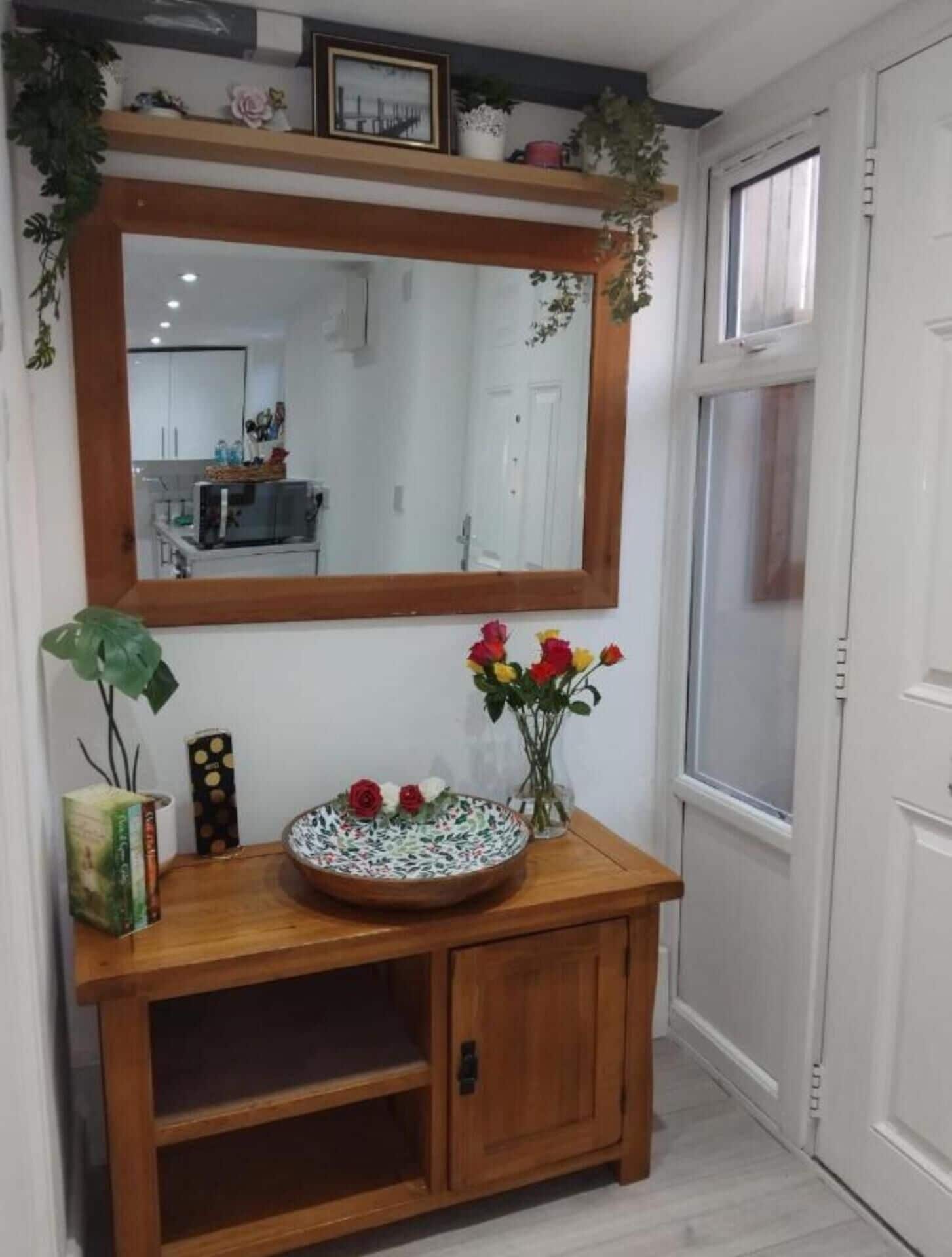 A wooden vanity with a mirror above it, a vase with flowers, and a potted plant beside the mirror.