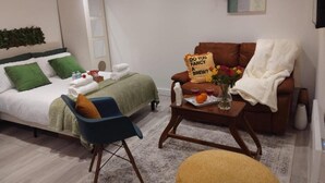 A modern bedroom with a bed, a blue chair, a brown sofa, and a small table with a vase and fruit.