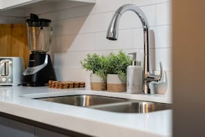 A kitchen with a stainless steel sink, a modern faucet, a toaster, and a blender on the counter.