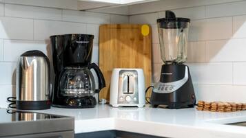 Una cocina con cafetera, licuadora, tostadora y tabla de cortar de madera.