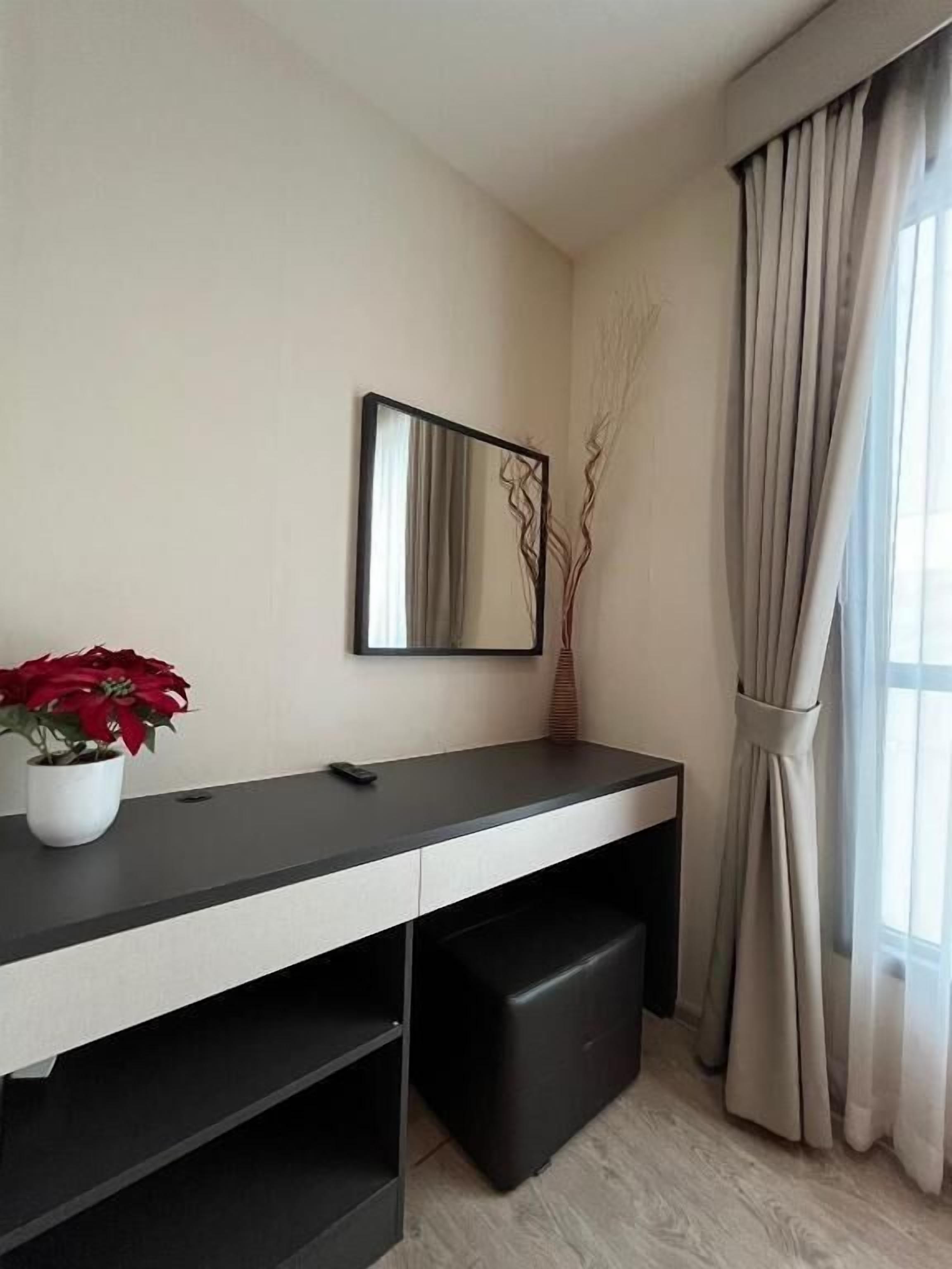 A modern room with a desk, a mirror, a potted plant, and a window with curtains.