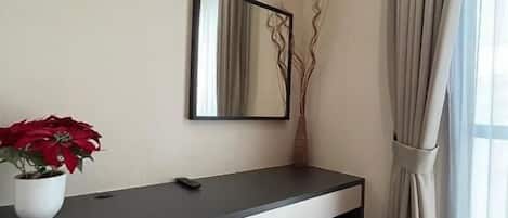 A modern room with a desk, a mirror, a potted plant, and a window with curtains.