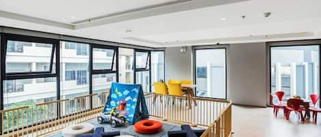 A spacious room with large windows, a play area with soft mats, and a view of the cityscape.