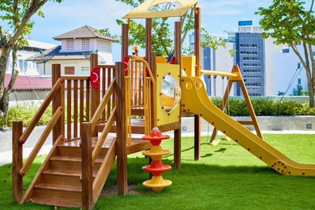 Un patio de juegos con un tobogán de madera y escaleras, rodeado de césped y árboles.