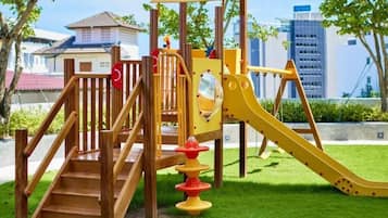 Un patio de juegos con un tobogán de madera y escaleras, rodeado de césped y árboles.
