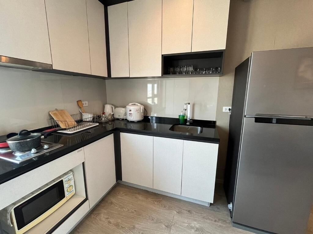 A kitchen with white cabinets, a black countertop, a built-in oven, a stainless steel refrigerator, and a shelf with glasses.