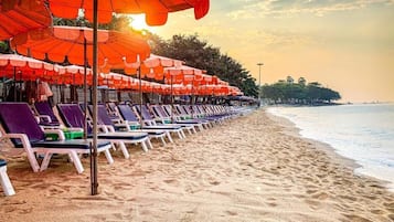 Une plage bordée de rangées de transats et de parasols, un rivage sablonneux et une mer calme.