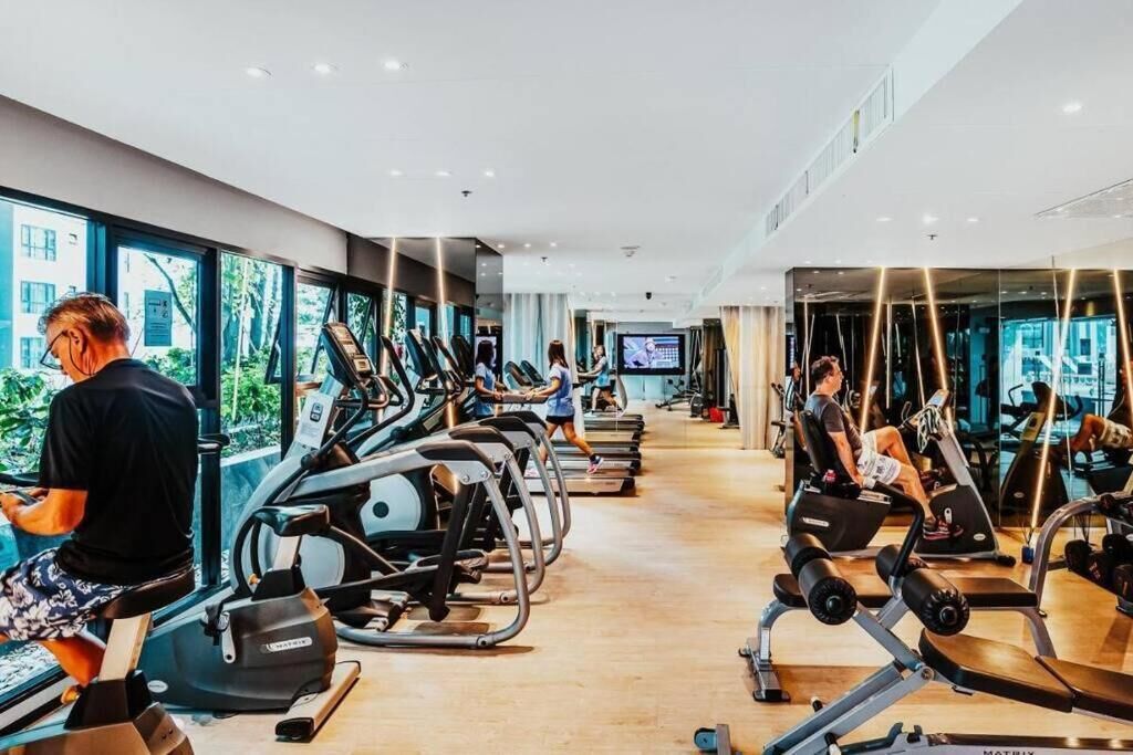 A gym with cardio machines and weightlifting equipment, large windows, and a TV screen.