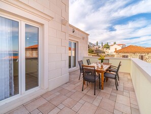 A balcony with a table and chairs, a view of the sea, and a stone building in the background. - Spacious Mediterranean 3-bedroom Apartment in Sutivan (Sutivan)