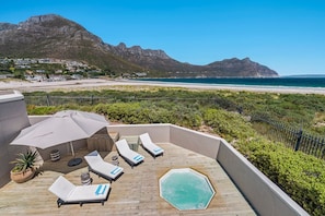 A rooftop deck with lounge chairs, a hot tub, and a view of the beach and mountains. - PINGU Beachhouse | Beachfront Villa with Hot Tub, Ocean Views & Beach Access (Cape Town)