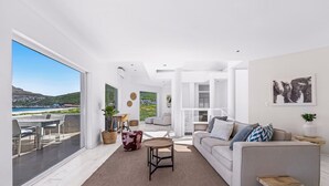 A modern living room with a large window, a sofa, a coffee table, and a view of the sea. - PINGU Beachhouse | Beachfront Villa with Hot Tub, Ocean Views & Beach Access (Cape Town)