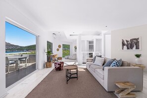 A modern living room with a large window, a sofa, a coffee table, and a view of the sea. - PINGU Beachhouse | Beachfront Villa with Hot Tub, Ocean Views & Beach Access (Cape Town)