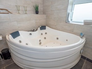 A modern bathroom with a large freestanding bathtub, a window, and a shelf with decorative items. - 4 Star Holiday Home in Vestervig (Vestervig)
