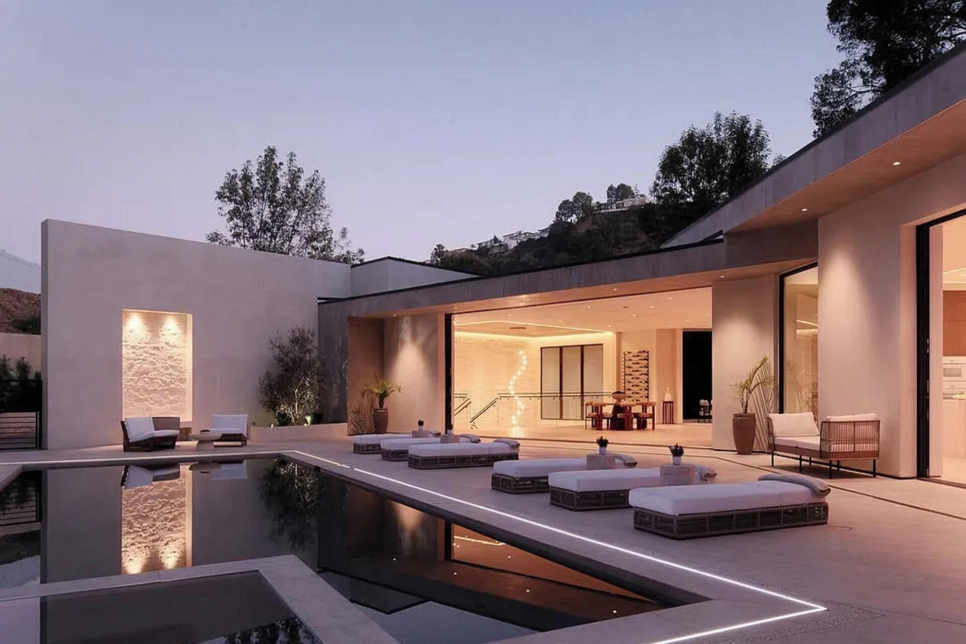 A modern house with a swimming pool, outdoor seating, and a well-lit interior.