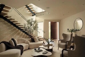 A modern living room with a staircase, a sofa, a coffee table, and a mirror. - Crown Ridge Estate - Exclusive Hollywood Hills Retreat | Resort-Style Living (Hollywood Hills)