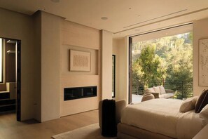 A modern bedroom with a large bed, a fireplace, a view of the outdoors, and a seating area with a table and chairs. - Crown Ridge Estate - Exclusive Hollywood Hills Retreat | Resort-Style Living (Hollywood Hills)