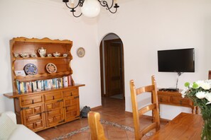 Ein Wohnzimmer mit Holzschrank, Fernseher und Esstisch.