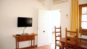 Une pièce dotée d’un téléviseur à écran plat fixé au mur, d’une table en bois avec des chaises et d’une porte blanche.