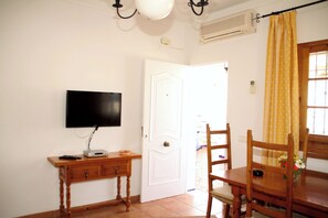 Ein Zimmer mit einem an der Wand befestigten Flachbildfernseher, einem Holztisch mit Stühlen und einer weißen Tür.
