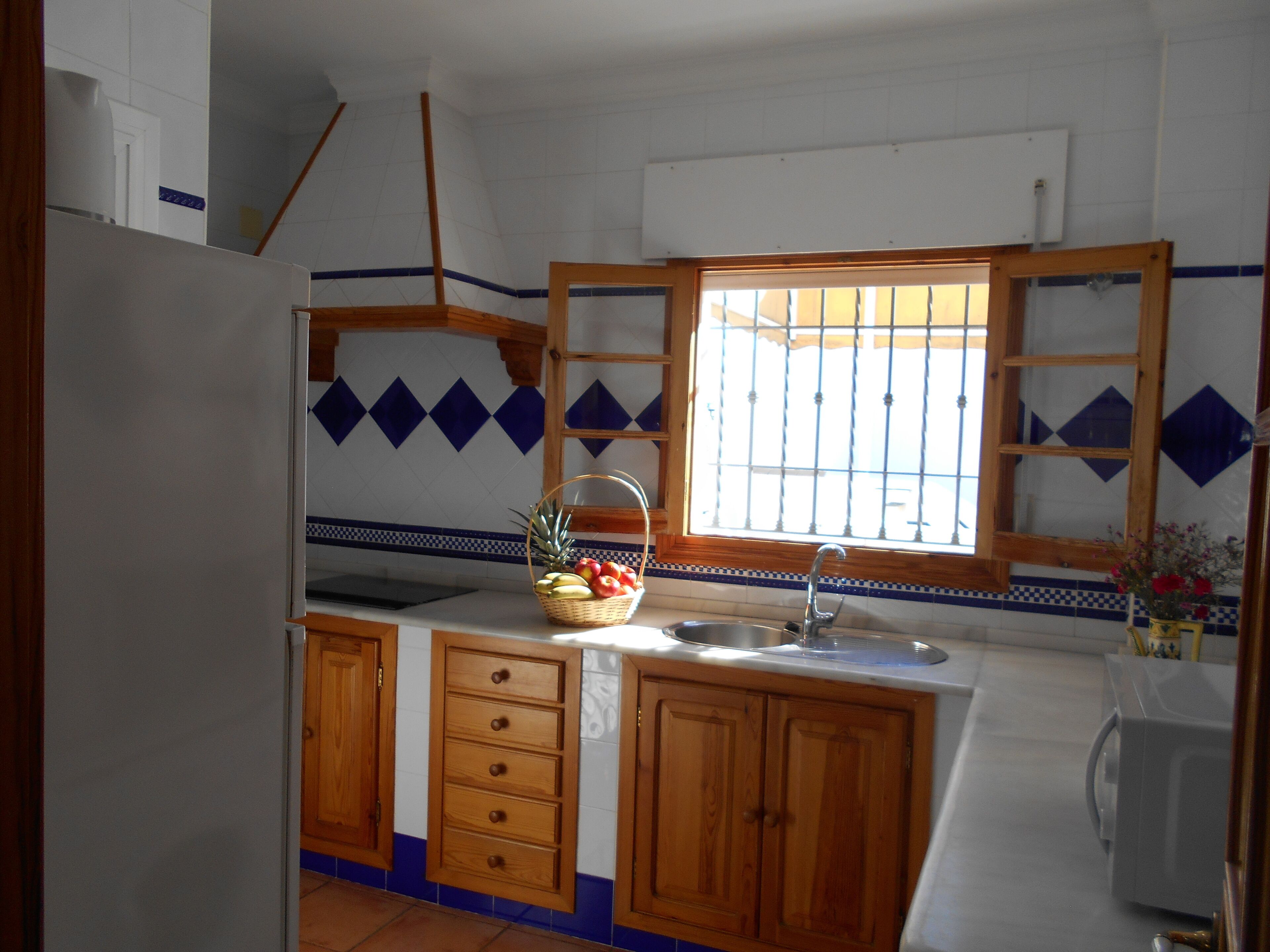 Una cocina con armarios de madera, un lavamanos y una ventana con rejas.