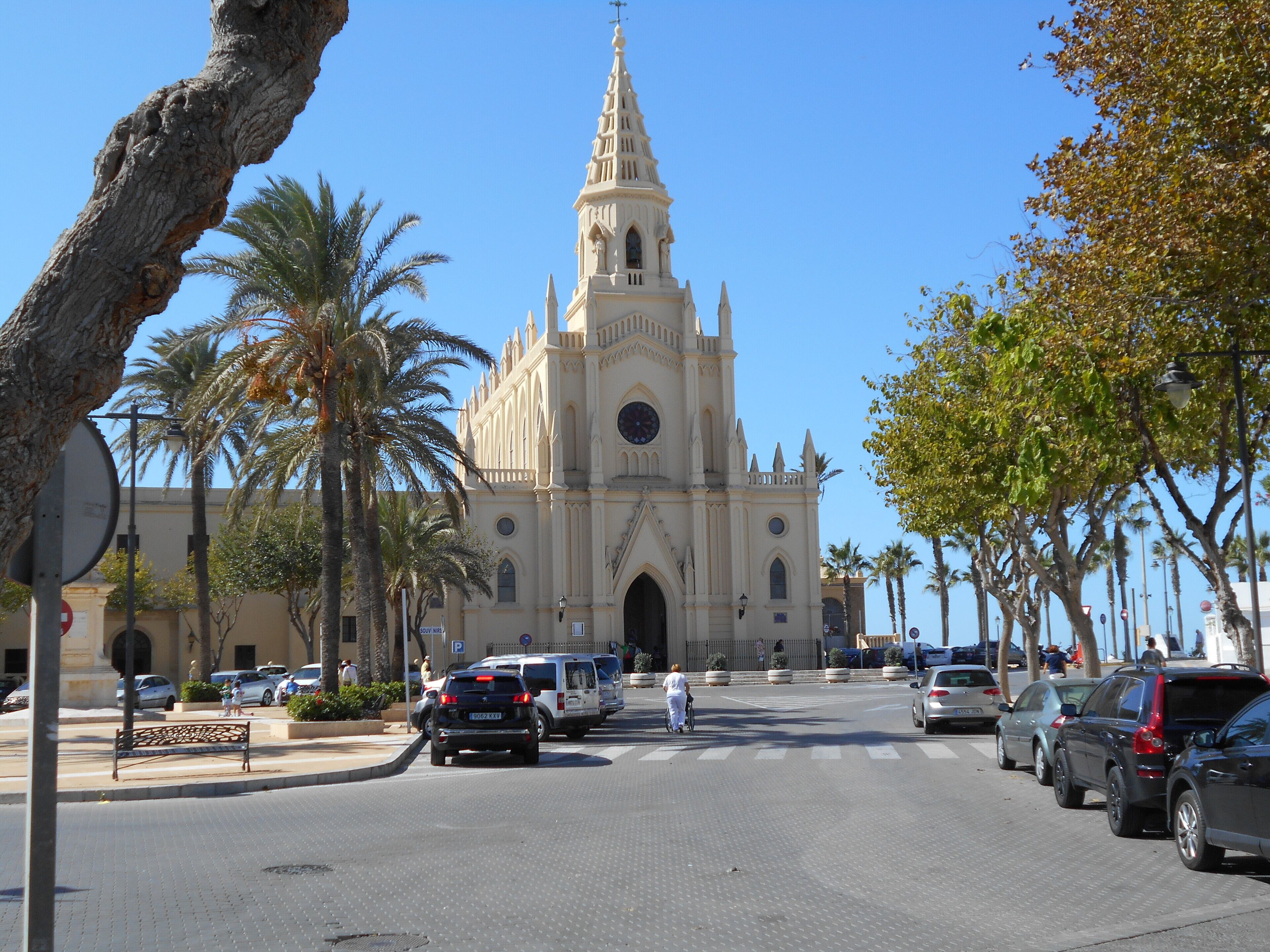 Une cathédrale dotée d’une haute flèche et d’une grande fenêtre circulaire, entourée de palmiers et bordée de voitures garées, le tout baigné par le soleil d’une belle journée.