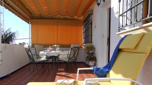 Une terrasse ensoleillée avec une table dressée pour deux personnes, un fauteuil de jardin jaune et une plante en pot.