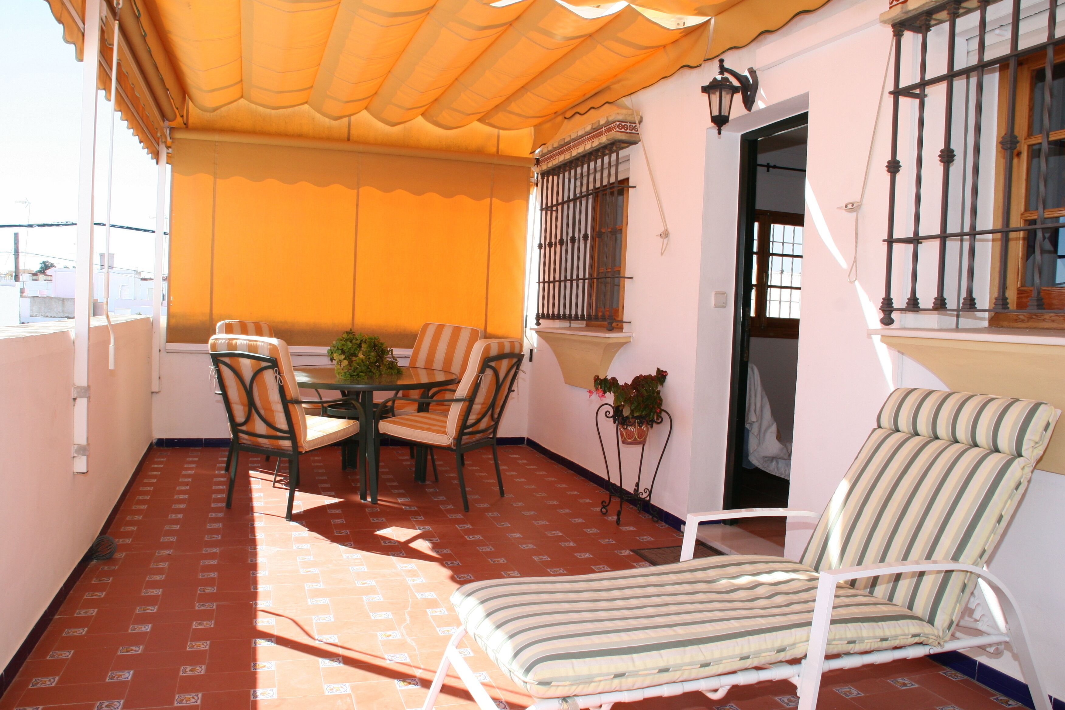Una veranda coperta con tavolo e sedie, una poltrona da esterno a righe e una pianta in vaso.
