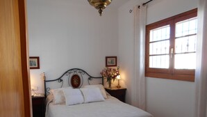 Une chambre à coucher avec un lit, une table de chevet, une lampe, une fenêtre avec des rideaux et une porte.