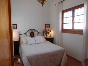 Ein Schlafzimmer mit einem Bett, einem Nachttisch, einer Lampe, einem Fenster mit Vorhängen und einer Tür.