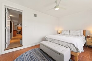 Ein Schlafzimmer mit Bett, Nachttischen, einer Bank, einem Deckenventilator und Blick auf den angrenzenden Wohnbereich.
