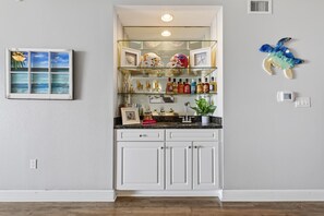 A kitchen with white cabinets, a countertop with various items, and a wall-mounted shelf with bottles and decorations. - Oceanfront Condo in Palm Coast Surf Club #317 (Palm Coast)